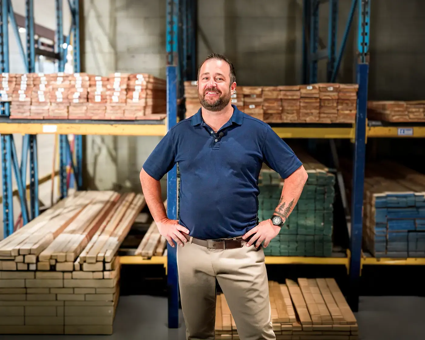 Kevin Martin standing hands-on-hips in a lumber yard, racks of stacked timber behind him