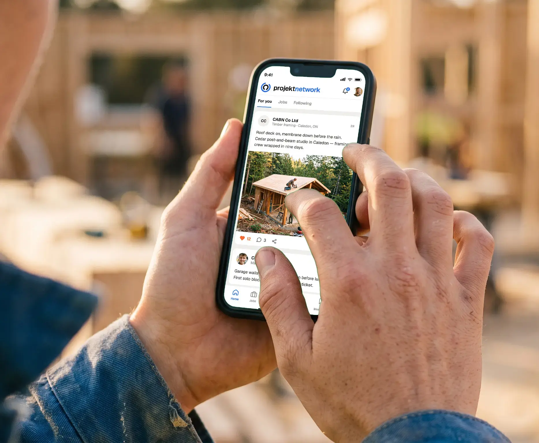 A tradesperson scrolling the Projekt Network feed on a phone in front of a timber frame